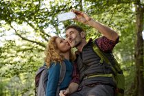 Pareja de senderismo tomando selfie con smartphone en el bosque - foto de stock
