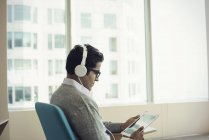Businessman sitting in chair, wearing headphones, using digital tablet — Stock Photo