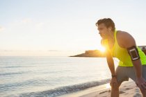 Giovane jogger che fa una pausa in spiaggia all'alba — Foto stock