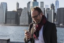 USA, Brooklyn, smiling businessman with earphones using smartphone — Stock Photo