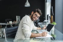 Портрет улыбающегося молодого человека, работающего с ноутбуком за столом в современном офисе — стоковое фото