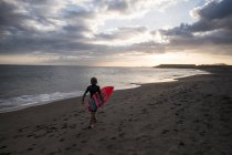 Visão traseira do adolescente carregando prancha de surf na praia — Fotografia de Stock