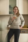 Mujer sonriente bebiendo jugo en la cocina - foto de stock