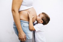 Petit garçon embrassant les mères enceintes ventre — Photo de stock