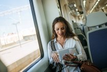 Smiling attractive caucasian woman on a train using a tablet — Stock Photo