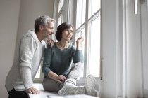 Pareja madura mirando por la ventana a casa - foto de stock