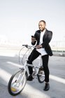 Uomo d'affari sorridente con bicicletta utilizzando il telefono cellulare — Foto stock