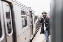 Молодой человек ждет метро на перроне вокзала с помощью смартфона — стоковое фото
