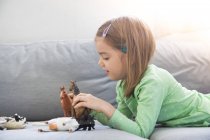 Bambina sdraiata sul divano e giocare con figurine animali — Foto stock