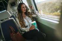 Жінка в поїзді, слухати музику з навушниками і пити каву — стокове фото