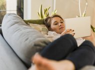 Young woman lying on couch and using tablet — Stock Photo