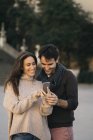Casal rindo compartilhando telefone celular ao ar livre — Fotografia de Stock