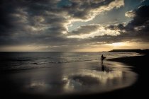 Spain, Tenerife, boy carrying surfboard on beach at sunset — Stock Photo