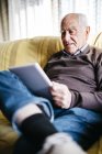 Старший чоловік, за допомогою планшетного ПК на дому в розслабленому стані, сидячи на дивані. — стокове фото