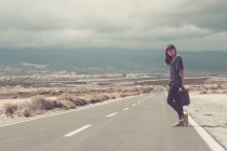 Giovane donna con valigia Autostop su strada — Foto stock