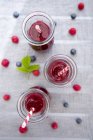 Three glasses of raspberry blueberry smoothies on grey surface with ingredients — Stock Photo
