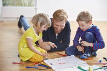 Father lying on floor with children painting — Stock Photo