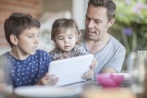 Padre y sus hijos mirando juntos a la tableta digital - foto de stock