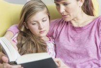 Madre e hija leyendo un libro juntas en casa - foto de stock