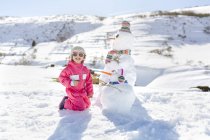 Cute caucasian girl playing with snowmen in winter — Stock Photo