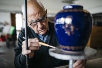 Старший человек украшает керамическую вазу в свободное время — стоковое фото
