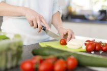 Vista recortada de la persona cortando tomates en la cocina - foto de stock