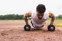 Athlete doing pushups with dumbbells on sports field — Stock Photo