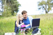 Батько і дочка, сидячи на полонині, батько працює на ноутбук — стокове фото