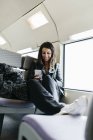 Sonriente mujer joven en tren mirando en el teléfono celular - foto de stock