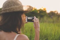 Vista posterior de la mujer tomando fotos con el teléfono inteligente en la naturaleza - foto de stock