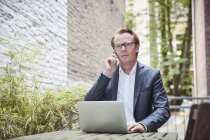 Telefonar a um empresário com um portátil sentado à mesa num quintal — Fotografia de Stock