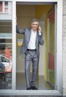 Empresário em pé na porta de seu escritório, segurando telefone celular — Fotografia de Stock