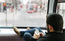 UK, London, young man in a double-decker bus using his smartphone — Stock Photo