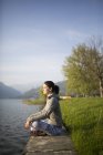 Italien, lecco, entspannte junge Frau sitzt am Seeufer — Stockfoto