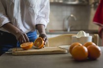 Mujer cortando naranjas sobre tabla de cortar de madera en la cocina - foto de stock