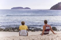 Indonesia, Isla de Sumbawa, Dos jóvenes sentados en la playa - foto de stock