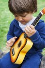Little cute boy playing guitar outdoors — Stock Photo
