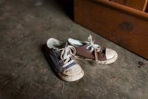 Pair of dirty child sneakers near wooden furniture — Stock Photo