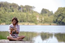 Giovane donna con tablet digitale seduta su un molo al lago — Foto stock
