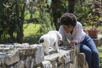 Donna che gioca con cane sul muro di pietra — Foto stock