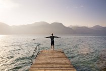Vista posteriore del ragazzo in piedi sul molo con le braccia tese — Foto stock