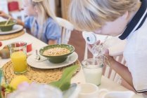 Garçon verser du lait dans le verre à la table du petit déjeuner — Photo de stock