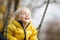 Boy wearing yellow jacket with eyes closed on swing — Stock Photo