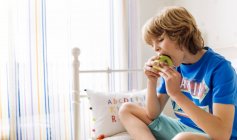 Portrait of boy sitting on the couch eating an apple — Stock Photo