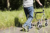 Back view of senior man strolling with wheeled walker in nature — Stock Photo