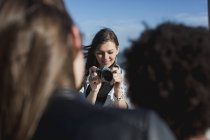 Молодая женщина с фотоаппаратом фотографирует друзей — стоковое фото