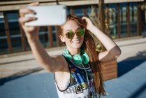 Sorrindo jovem mulher vestindo óculos de sol espelhados levando selfie com smartphone — Fotografia de Stock