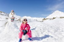 Mignon caucasien fille assis en face de bonhomme de neige — Photo de stock