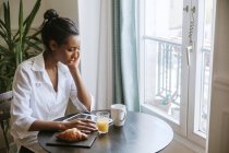 Молода жінка, використовуючи цифровий планшетний сніданок столом — стокове фото