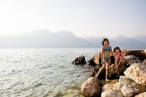 Italia, Brenzone, Dos hermanas de pie en roca a orillas del lago - foto de stock